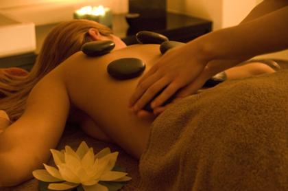 Hot stone massage on the back, beside a lotus flower and a candle